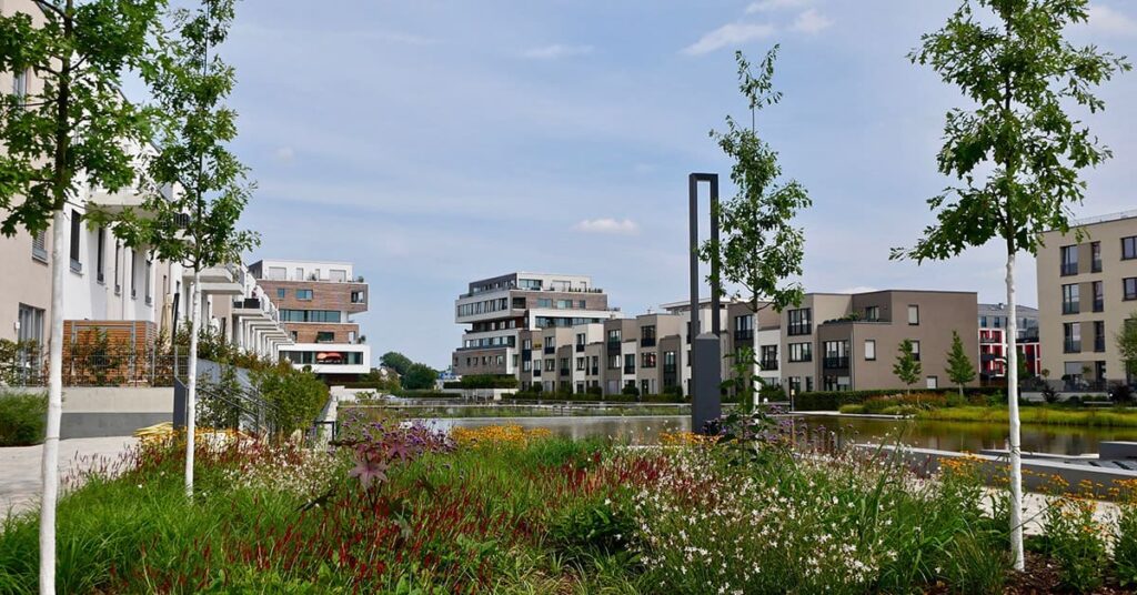 Grünfläche mit Blüten und Bäumen an der künstlichen Wasserfläche