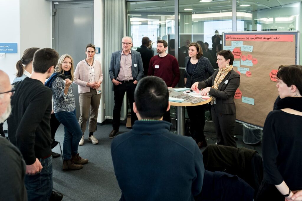 mehrere Personen in einem Kreis vor einer Pinnwand im Gespräch