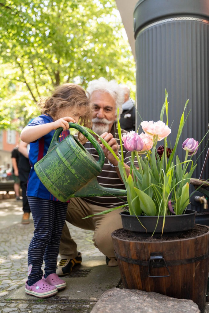 Kind gießt einen Blumenkübel neben einer Regentonne