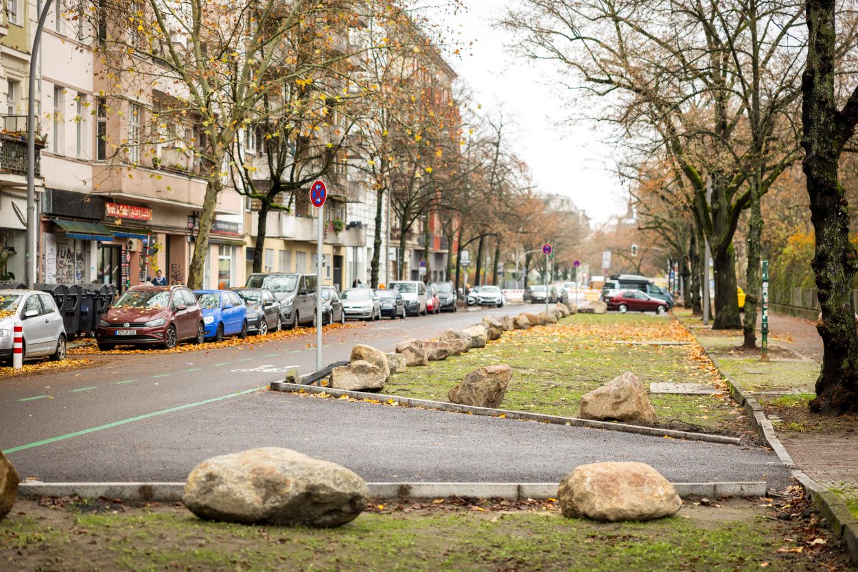 Die Fahrbahn wurde auf einer Seite fast über die gesamte Länge bis zur Straßenmitte aufgebrochen, begrünt und durch große Findlinge vor Parkenden Autos geschützt.