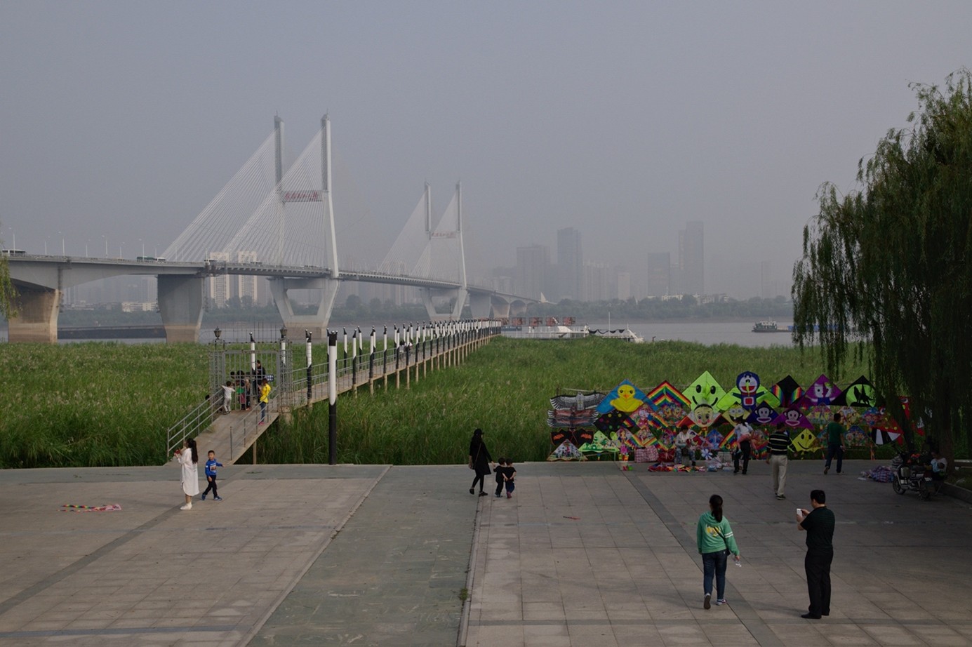 Eine der größten Ufergrünflächen Asiens. Grün dienen im Hankou Jiangtan Park, auch Yangtse Riverfront Park genannt, als Erholungsfläche und zum Hochwasserschutz. Im Hintergrund ist eine große Brücke zu sehen.