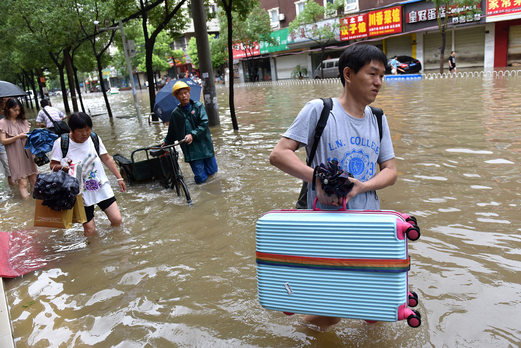Überflutung in Wuhan 2016. Personen tragen ihr Hab und Gut durch kniehohes Wasser in der Stadt.